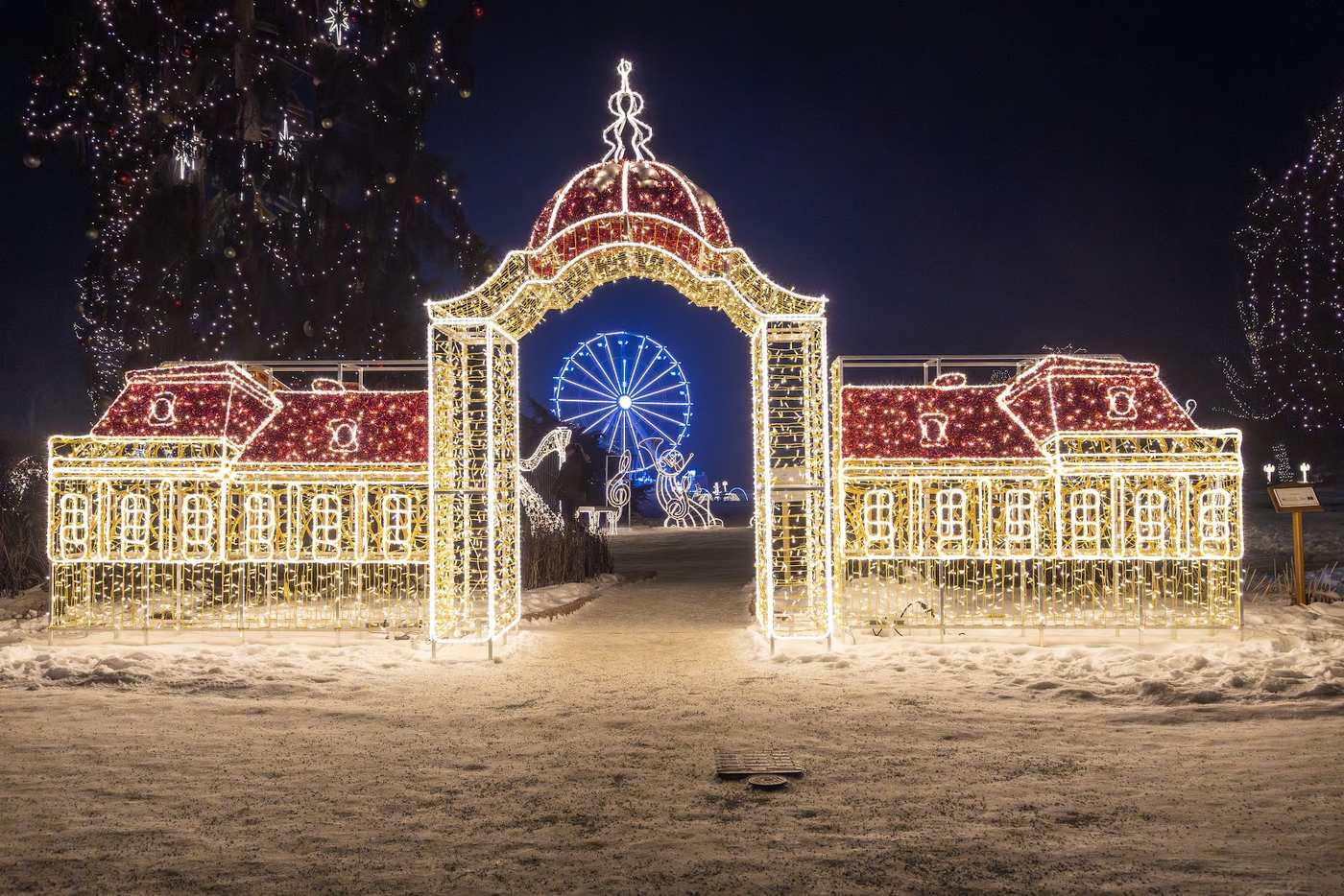 A broad light sculpture of a baroque palace with a red roof, a ferris wheel glowing through the central arch
