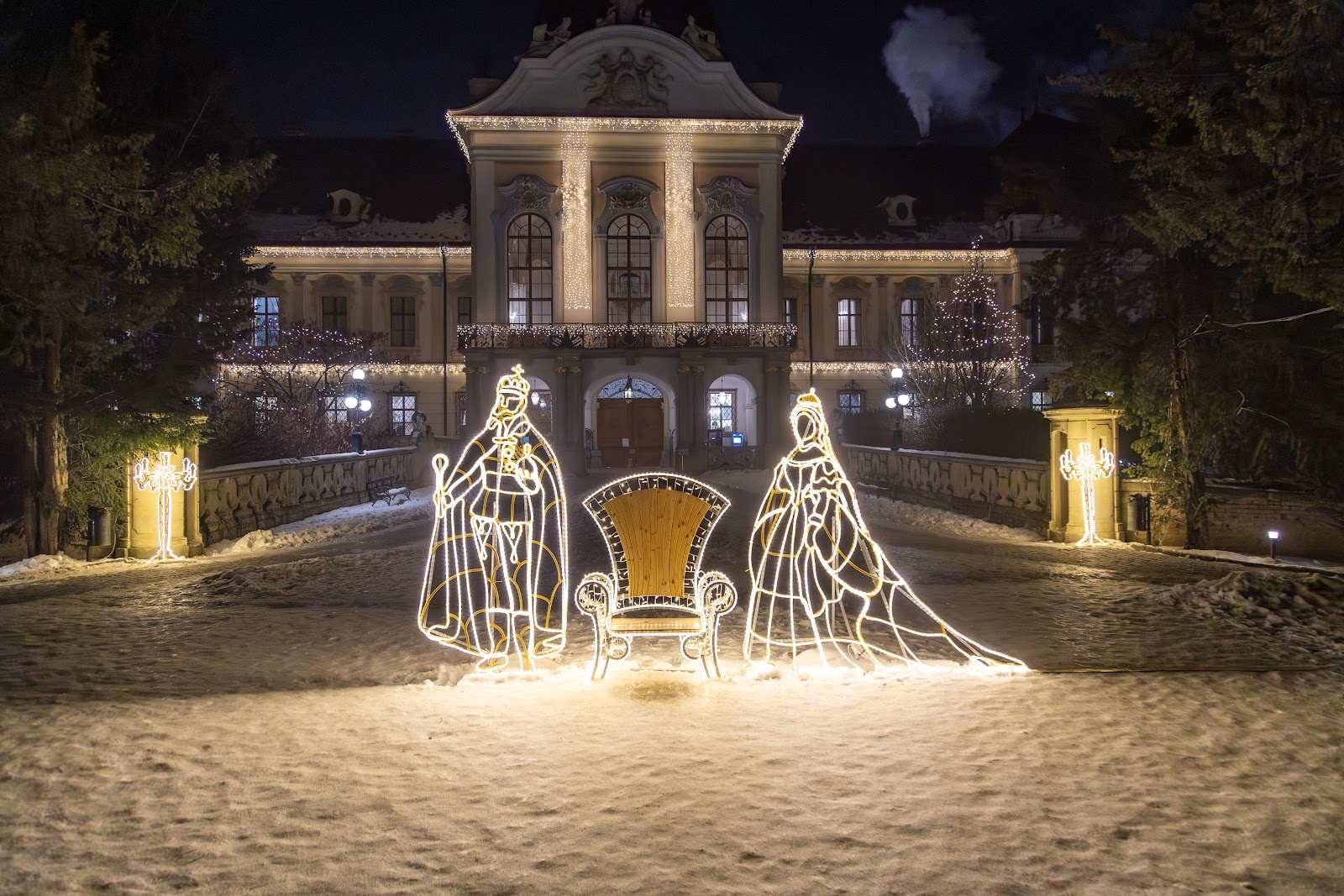 The lit palace facade with a throne and two seated figures of light in front of it