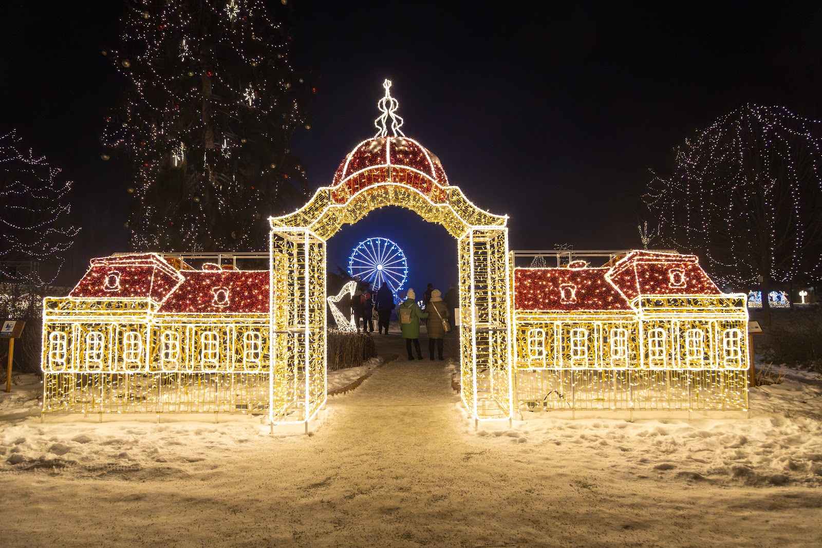 A light sculpture built as a wide palace facade with a red roof, a ferris wheel glowing through its central arch