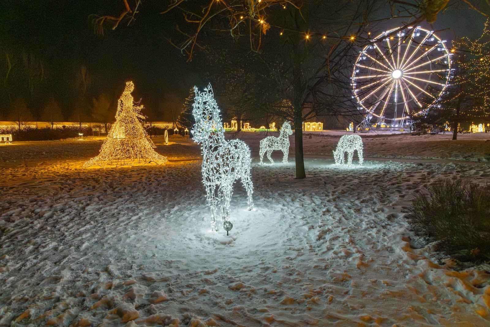 A white horse sculpture of light on snow, a blue ferris wheel in the distance