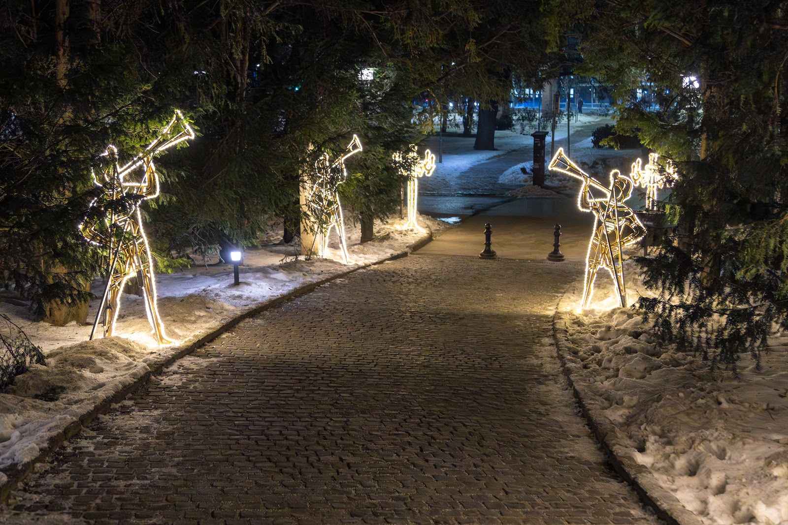 Three trumpeter figures made of light standing along a dark park path